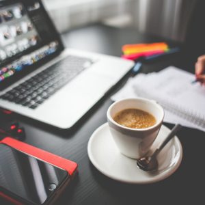 Coffee-filled Cup on Saucer Beside Macbook and Iphone on Desk