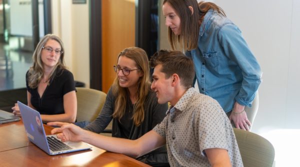 A group of people sitting at a table using a computer  Description automatically generated