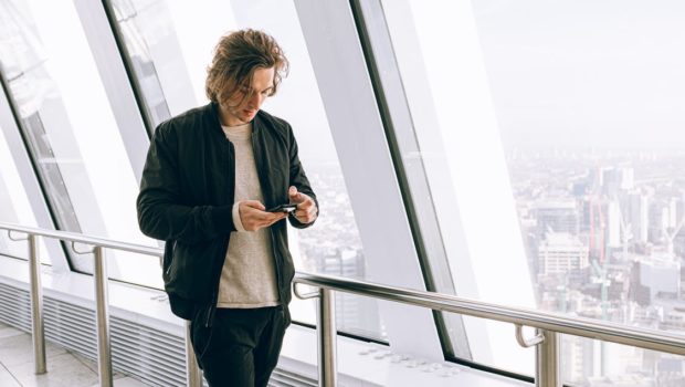 Man in Black Jacket Walking Beside Large Window