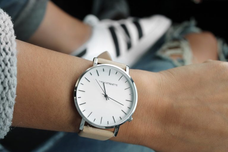 Beige Strap Silver Round Analog Watch Behind Adidas White and Black Superstar