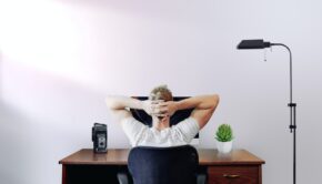 man holding his head while sitting on chair near computer desk