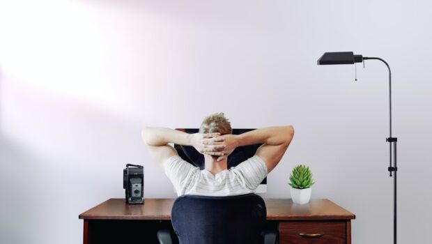 man holding his head while sitting on chair near computer desk